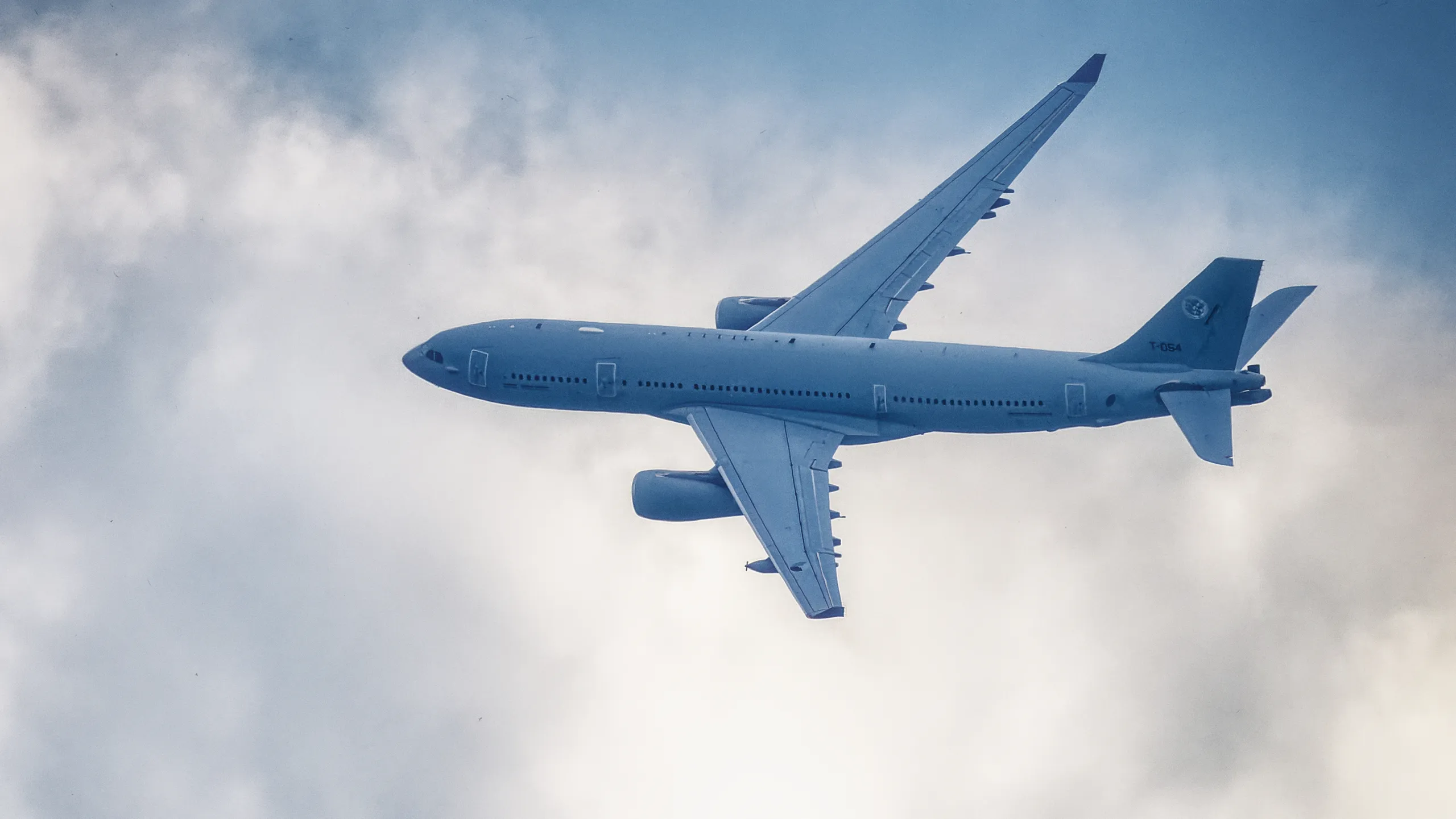 Airbus A330 MRTT mit der Kennung T-054 im Flug, von unten fotografiert vor einer hellen Wolkenlandschaft.
