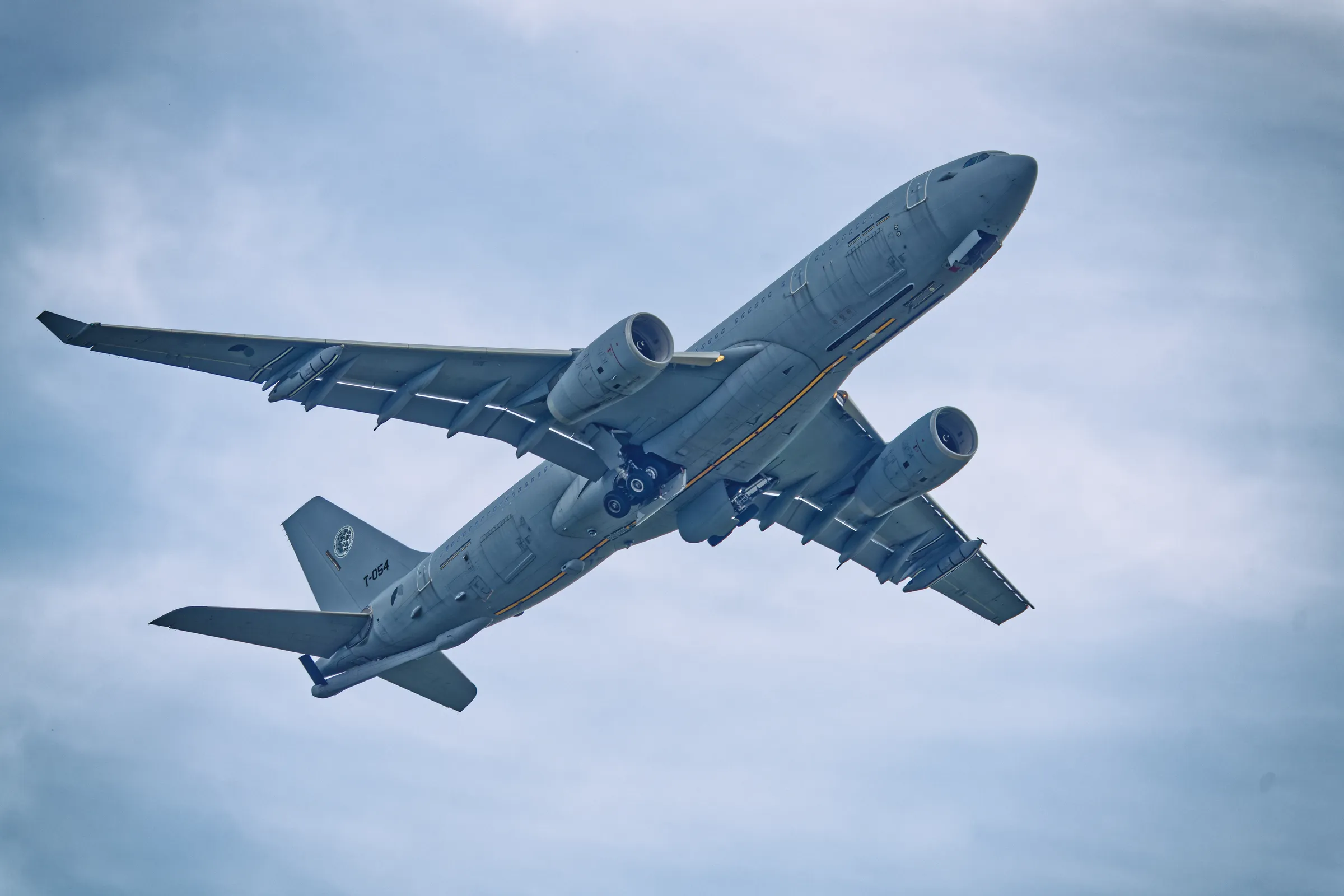 Airbus A330 MRTT mit der Kennung T-054 im Überflug, von unten fotografiert mit sichtbaren Triebwerken und teilweise ausgefahrenem Fahrwerk.
