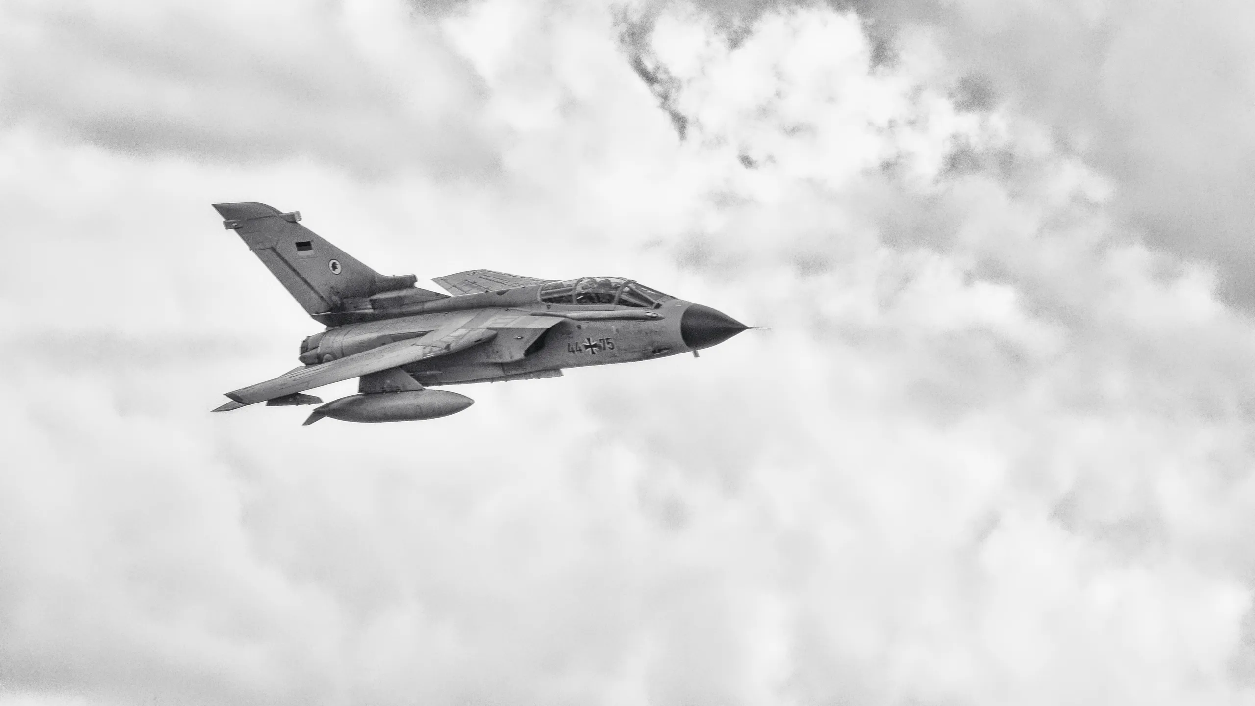 Schwarzweißaufnahme eines Panavia Tornado der Bundeswehr mit der Kennung 44+75 im Flug vor einer hellen Wolkenlandschaft.