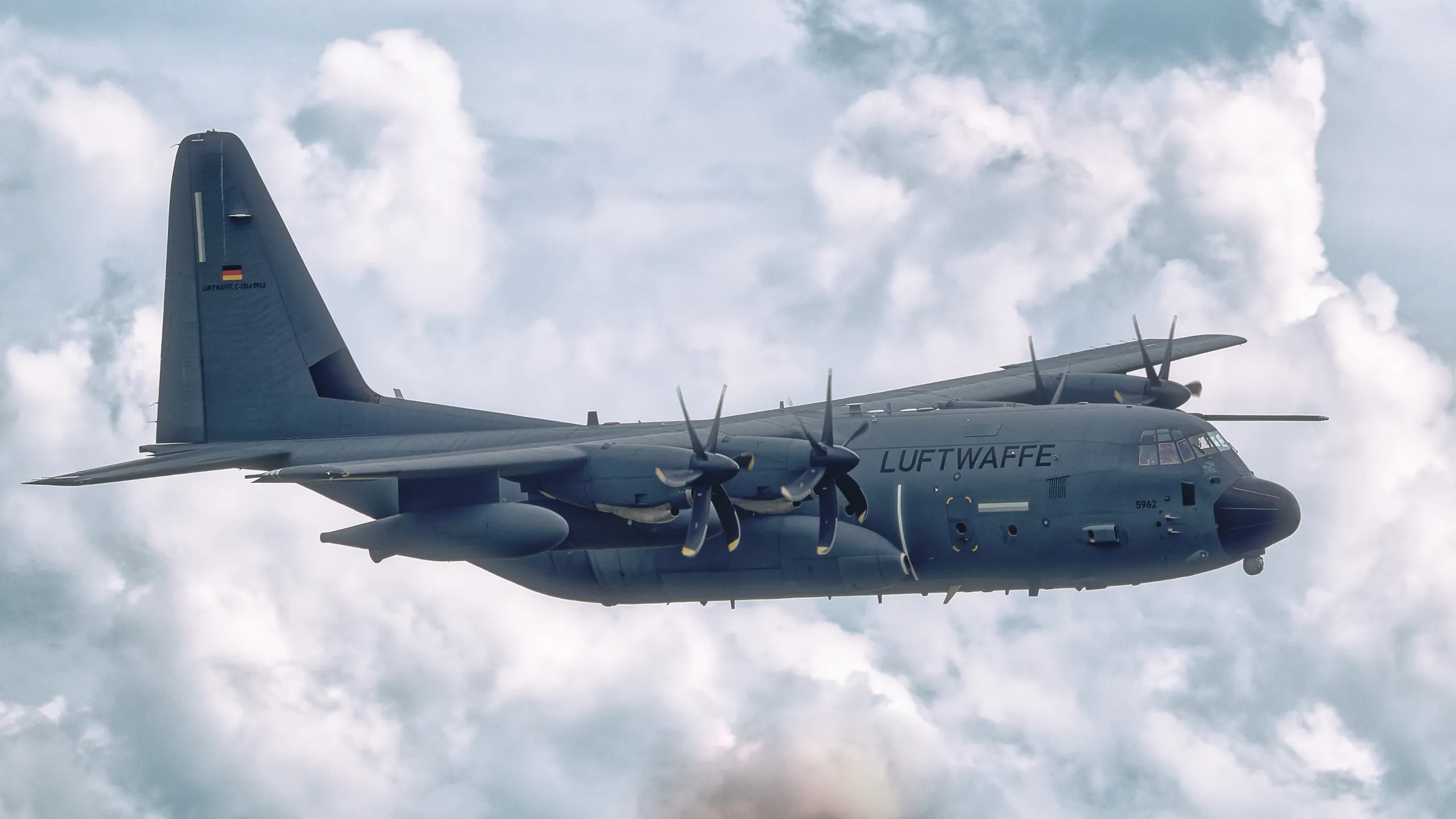 Transall C-130J der Bundeswehr im Seitenflug vor einer hellen Wolkenlandschaft, mit zwei deutlich erkennbaren Propellertriebwerken.