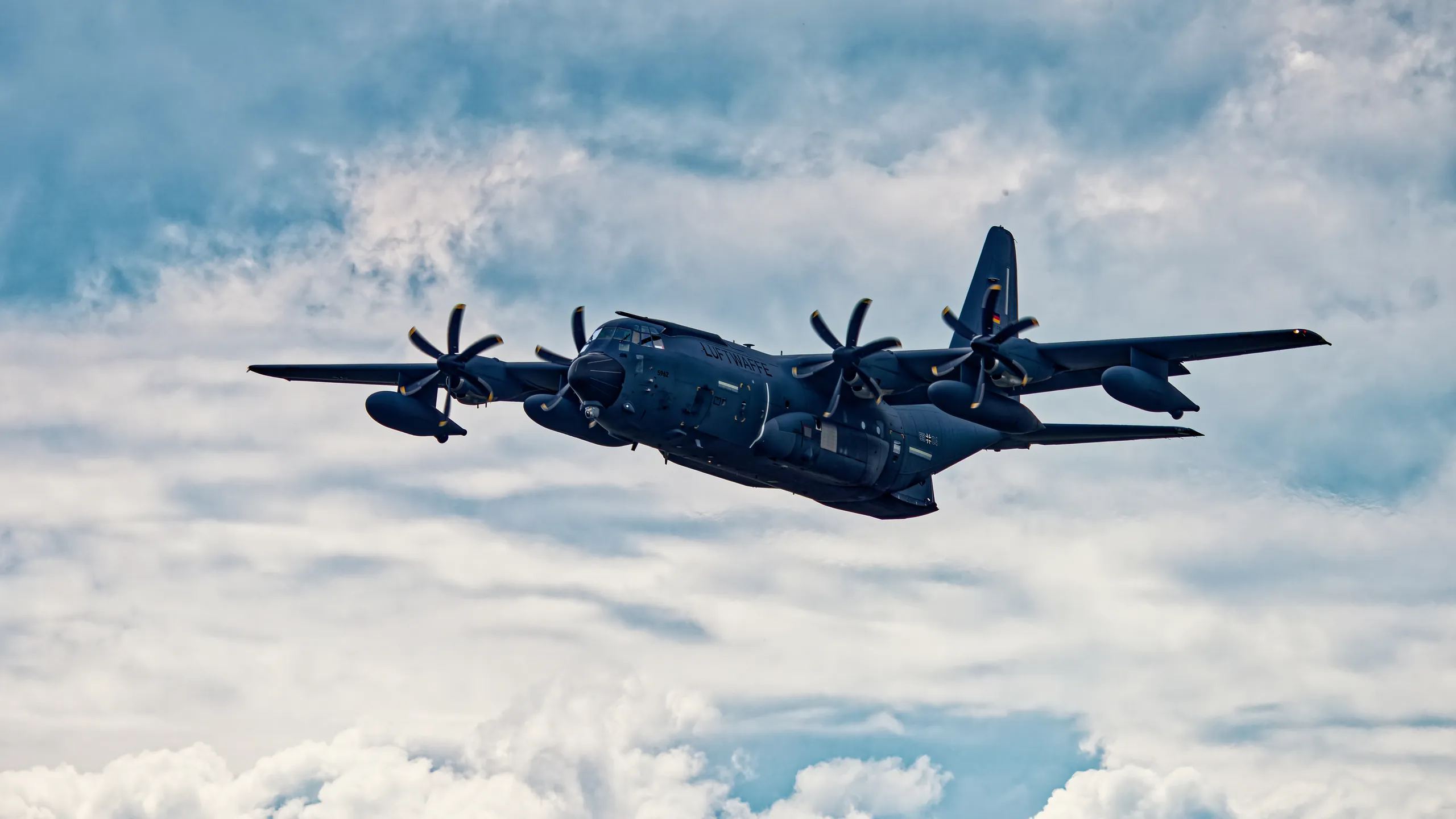 Viermotoriges Transportflugzeug C-130J der deutschen Luftwaffe im Flug vor einem bewölkten Himmel, aus leicht schräger Perspektive fotografiert.