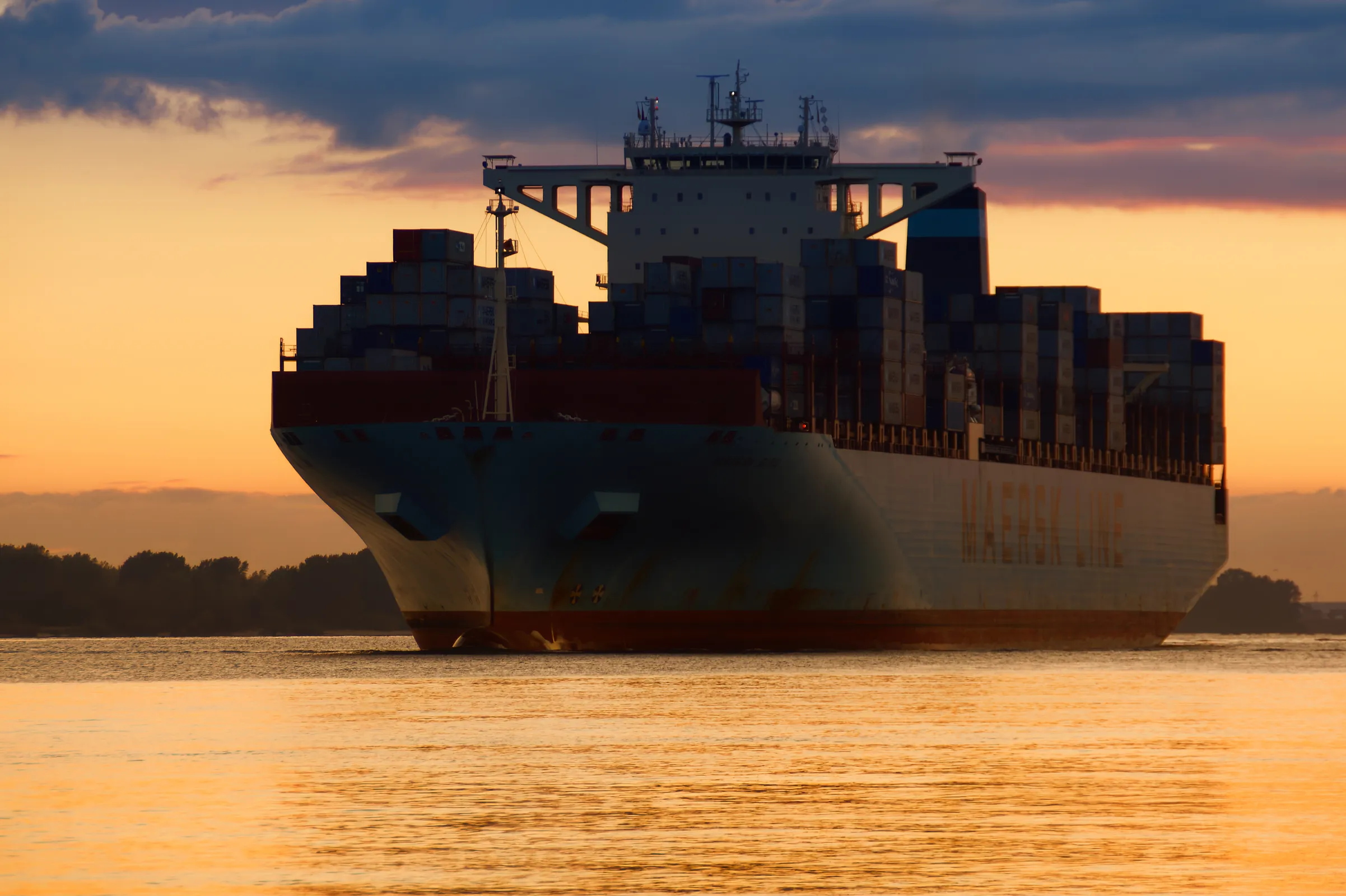 Großes Containerschiff der Reederei Maersk fährt bei goldenem Sonnenuntergang über die Elbe bei Hamburg.