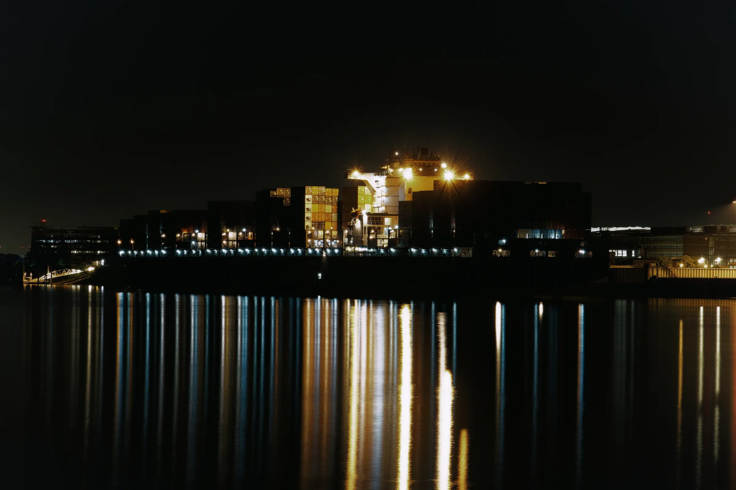 Beleuchtetes Containerschiff bei Nacht im Hamburger Hafen mit langen Lichtreflexionen auf dem dunklen Wasser.