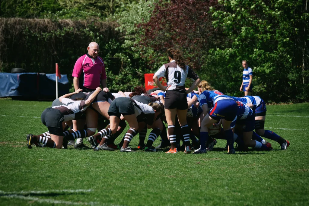 Die Damenrugby-Mannschaften des FC St. Pauli und Bayern München kämpfen in einem Gedränge um den Rugbyball, während der Schiedsrichter die Spielsituation überwacht.