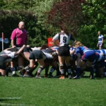 Die Damenrugby-Mannschaften des FC St. Pauli und Bayern München kämpfen in einem Gedränge um den Rugbyball, während der Schiedsrichter die Spielsituation überwacht.