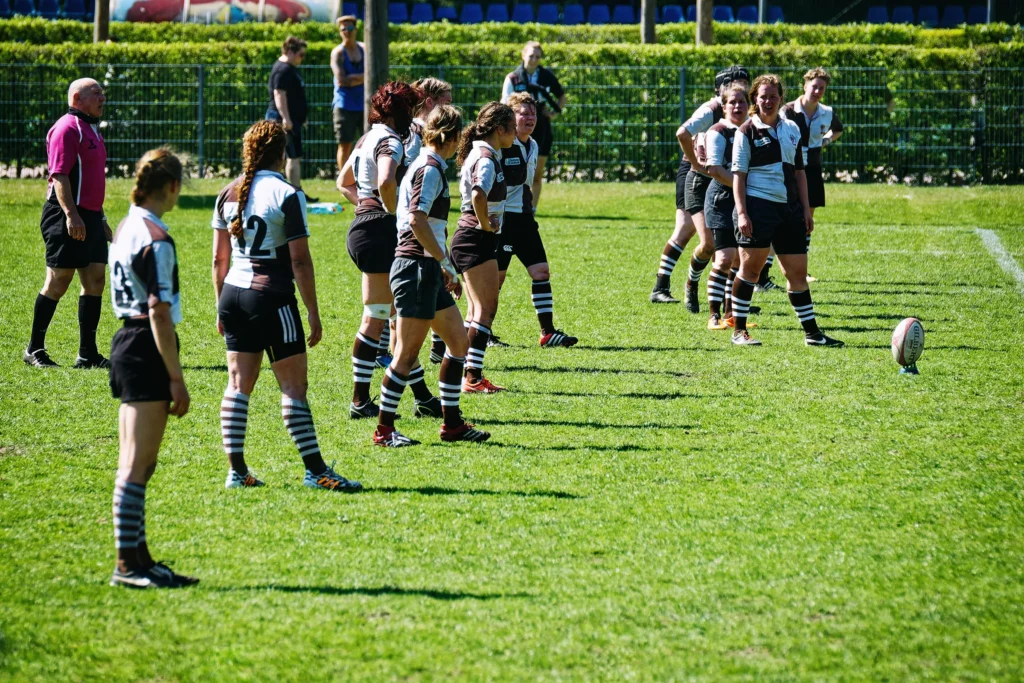 Rugbyspielerinnen des FC St. Pauli in braun-weißen Trikots bereiten sich auf einen ruhenden Kick gegen Bayern München vor, während der Rugbyball auf dem Rasen steht.