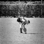 Schwarz-Weiß-Fotografie einer Rugbyspielerin des FC St. Pauli, die sich nach vorne beugt und den Rugbyball für einen Kick gegen Bayern München positioniert.