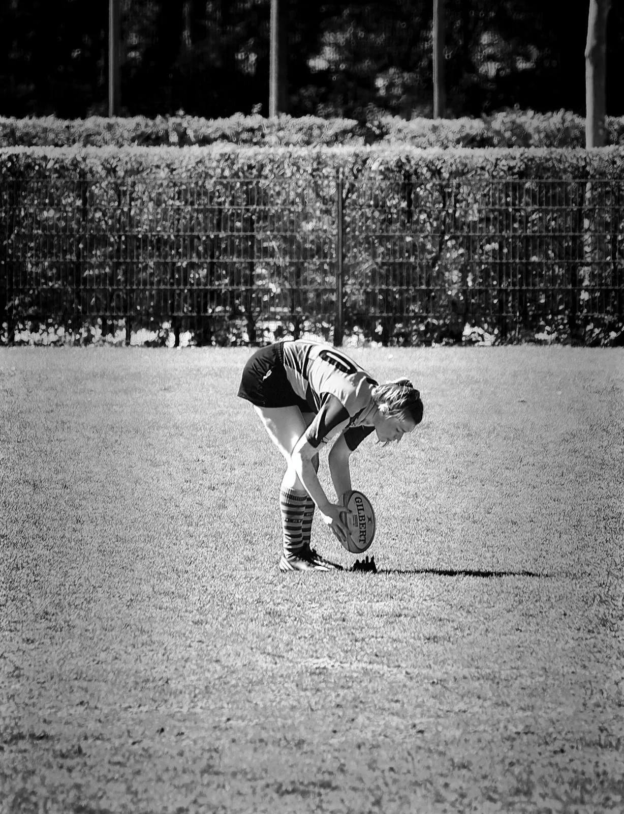 Schwarz-Weiß-Fotografie einer Rugbyspielerin des FC St. Pauli, die sich nach vorne beugt und den Rugbyball für einen Kick gegen Bayern München positioniert.
