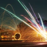 Spektakulärer Funkenregen aus brennender Stahlwolle mit goldenen Lichtbögen und bunten Lichtspuren während einer Langzeitbelichtung.