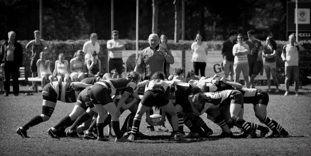 Schwarz-Weiß-Aufnahme eines intensiven Gedränges beim Damenrugby zwischen dem FC St. Pauli und Bayern München mit zahlreichen Spielerinnen und einem Schiedsrichter im Hintergrund.