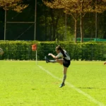 Rugbyspielerin des FC St. Pauli im braun-weißen Trikot tritt den Rugbyball mit ausgestrecktem Bein über das Spielfeld im Spiel gegen Bayern München.