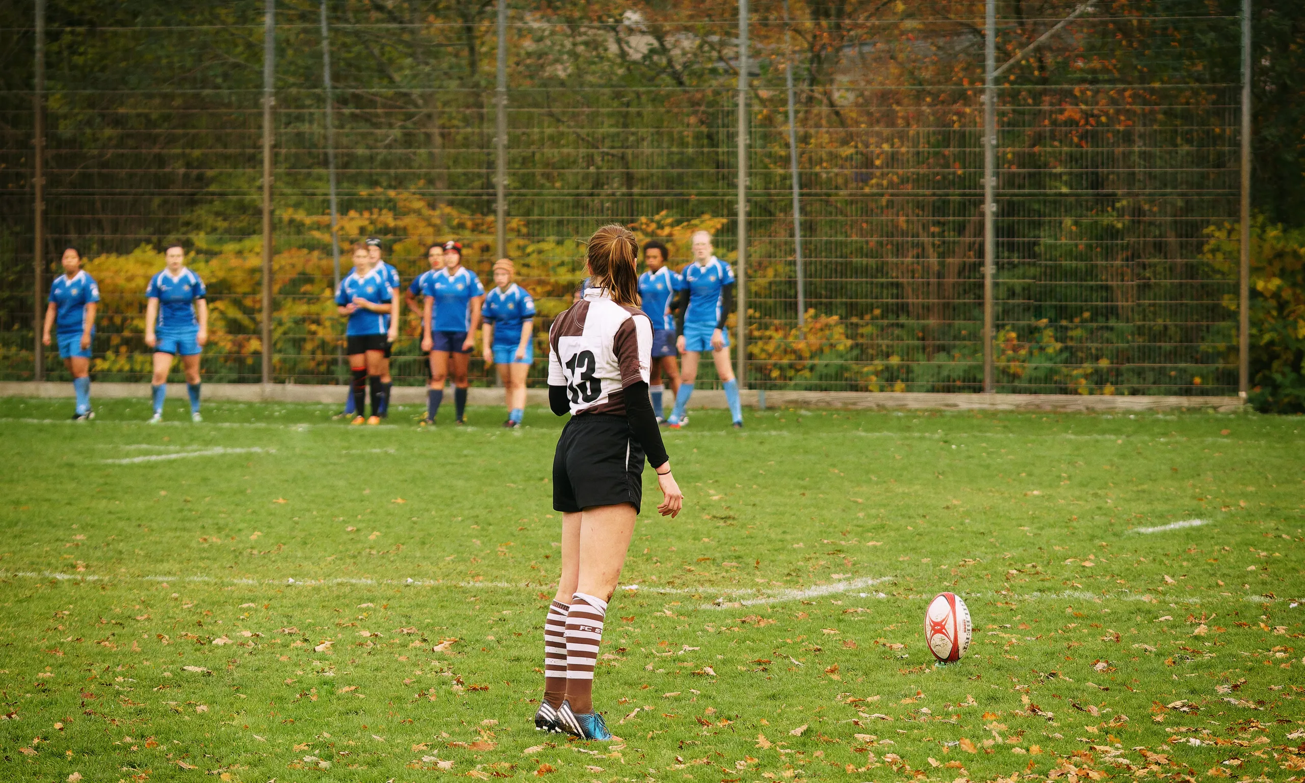Damenrugby-Spielerin des FC St. Pauli mit der Rückennummer 13 steht vor einem ruhenden Rugbyball und bereitet einen Kick gegen Bayern München vor.