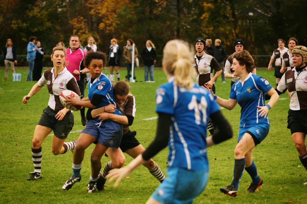Rugbyspielerin von Bayern München im blauen Trikot wird während eines Angriffs von einer Gegenspielerin des FC St. Pauli umklammert und gestoppt.