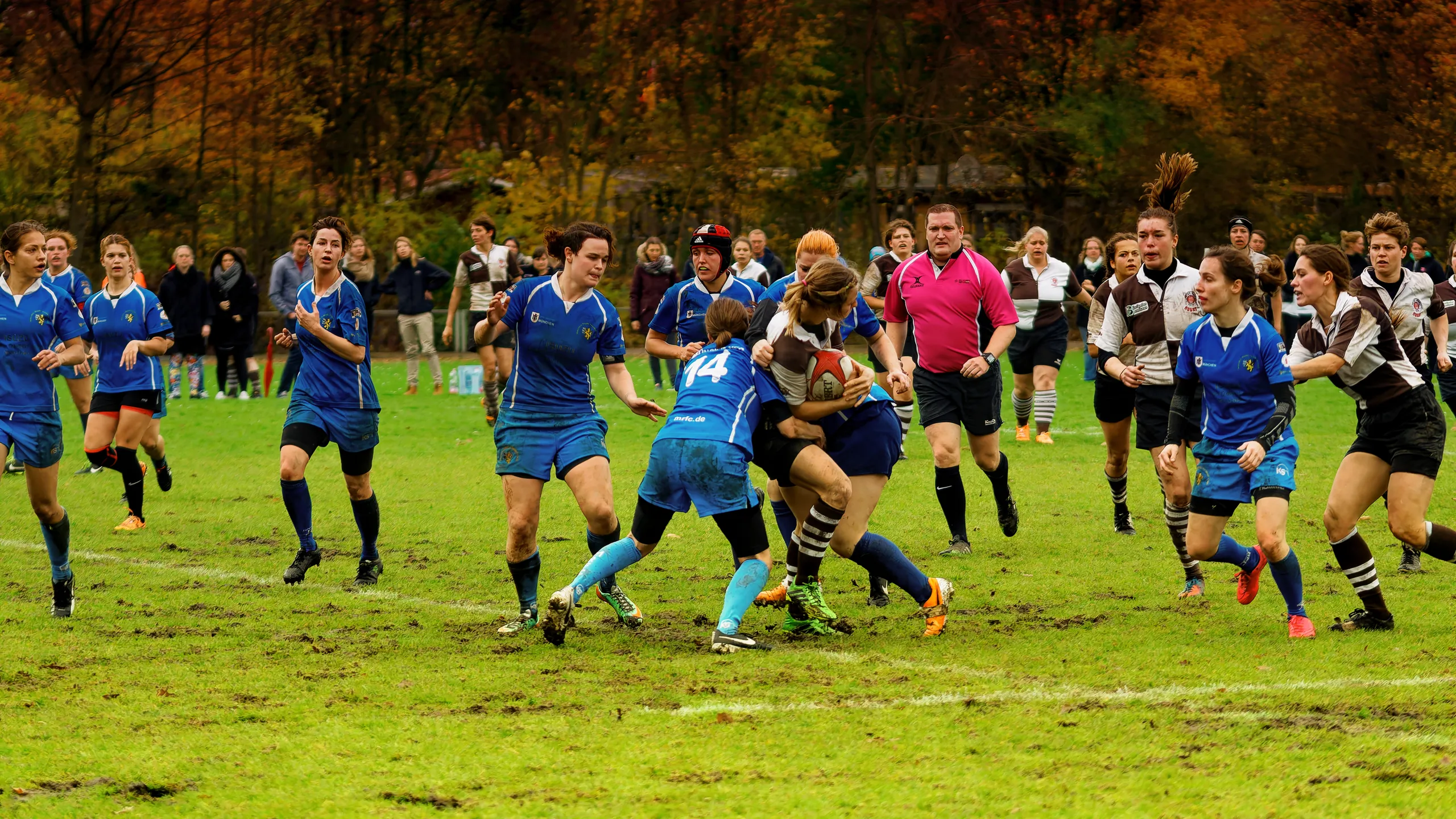 Dynamische Damenrugby-Szene zwischen dem FC St. Pauli und Bayern München, während eine Ballträgerin von St. Pauli durch eine Gegenspielerin in Blau angegriffen wird.