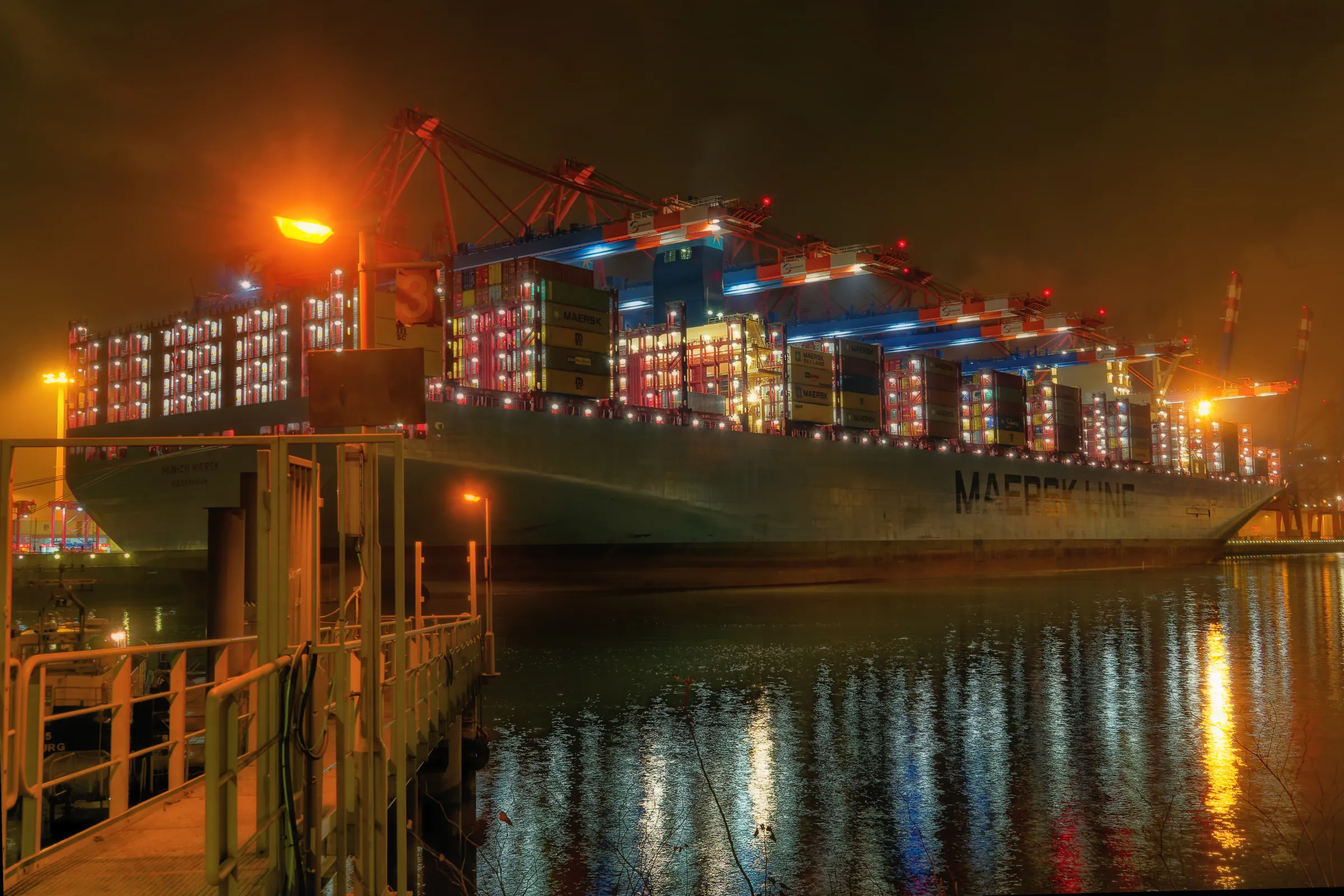 Gewaltiges Containerschiff der Reederei Maersk liegt nachts an einem beleuchteten Containerterminal im Hamburger Hafen.