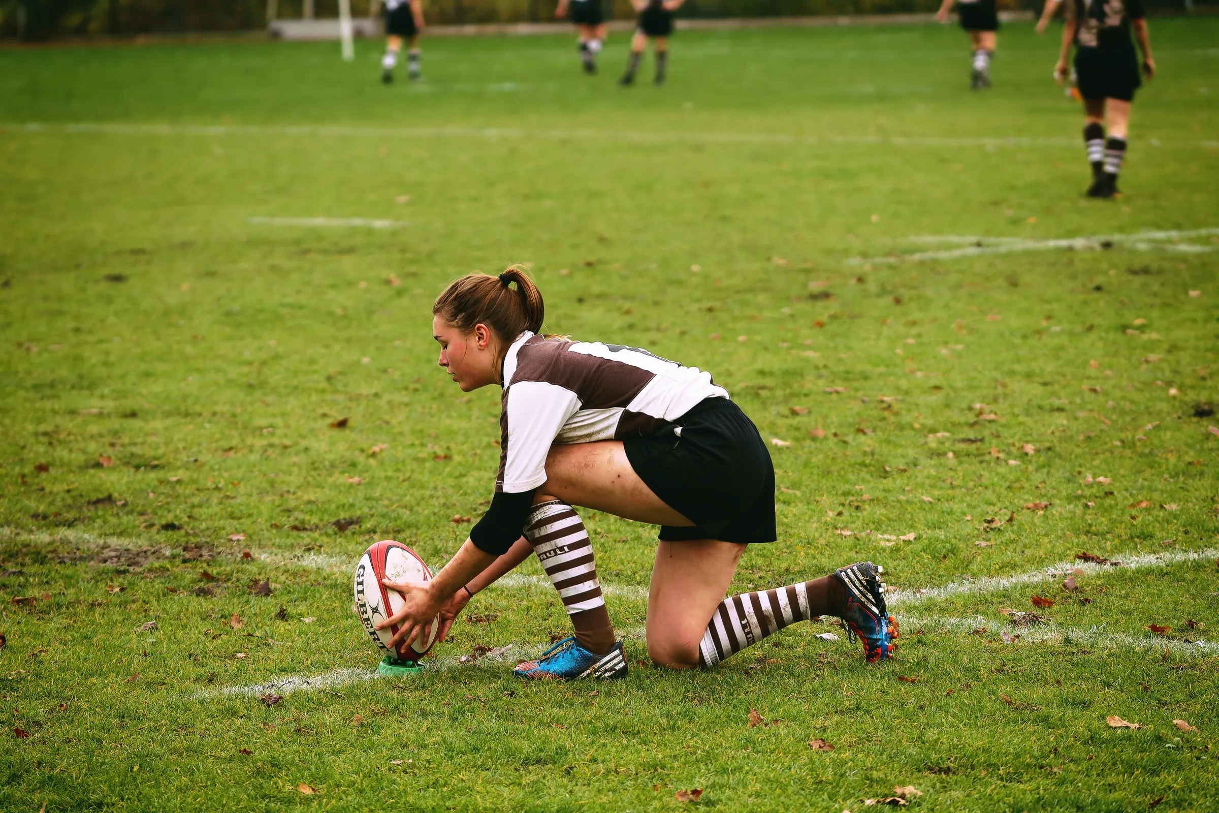 Rugbyspielerin des FC St. Pauli kniet auf dem Rasen und platziert den Rugbyball für einen ruhenden Kick im Spiel gegen Bayern München.