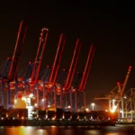 Rot beleuchtete Containerbrücken und ein großes Containerschiff am Containerterminal Altenwerder im Hamburger Hafen bei Nacht.