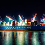 Großes blaues Containerschiff von COSCO Shipping bei nächtlichen Verladearbeiten unter beleuchteten Containerbrücken im Hamburger Hafen.