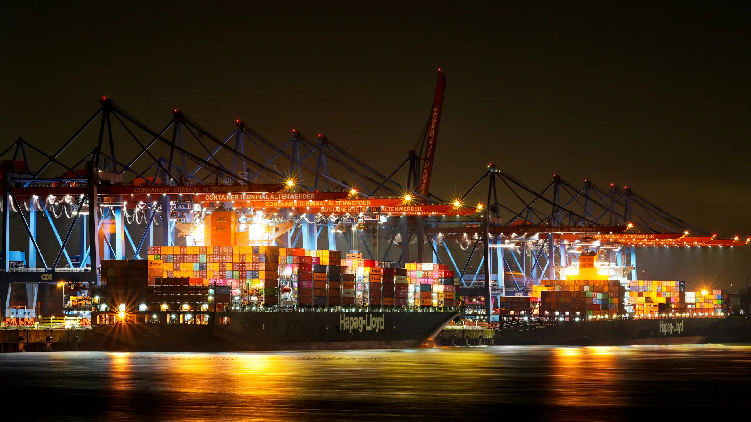 Beleuchtete Containerschiffe von Hapag-Lloyd am Containerterminal Altenwerder im Hamburger Hafen bei Nacht.