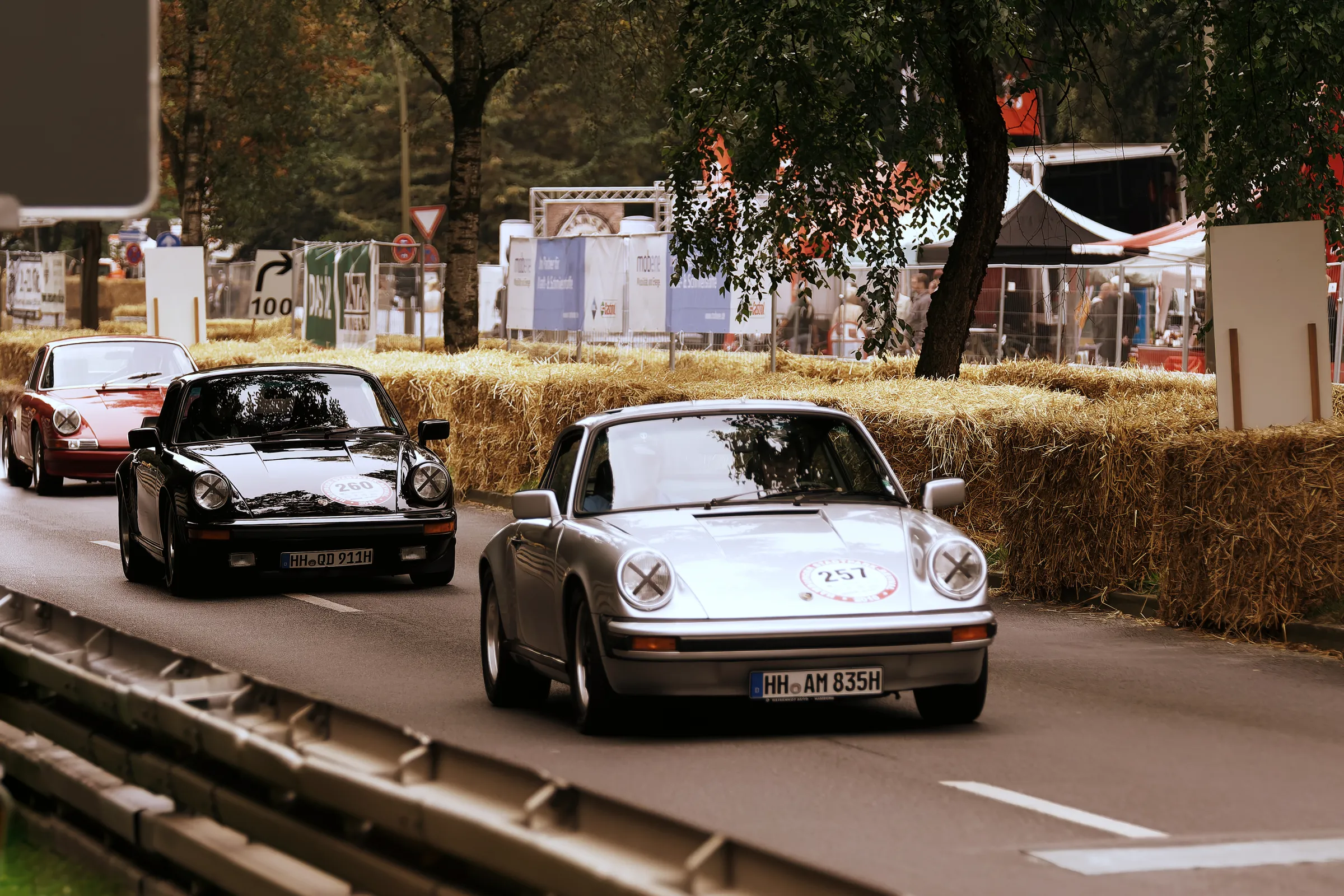 Silberner Porsche 911 G-Modell mit Startnummer 257 vor einem schwarzen und einem roten klassischen Porsche 911 beim Stadtpark-Revival.