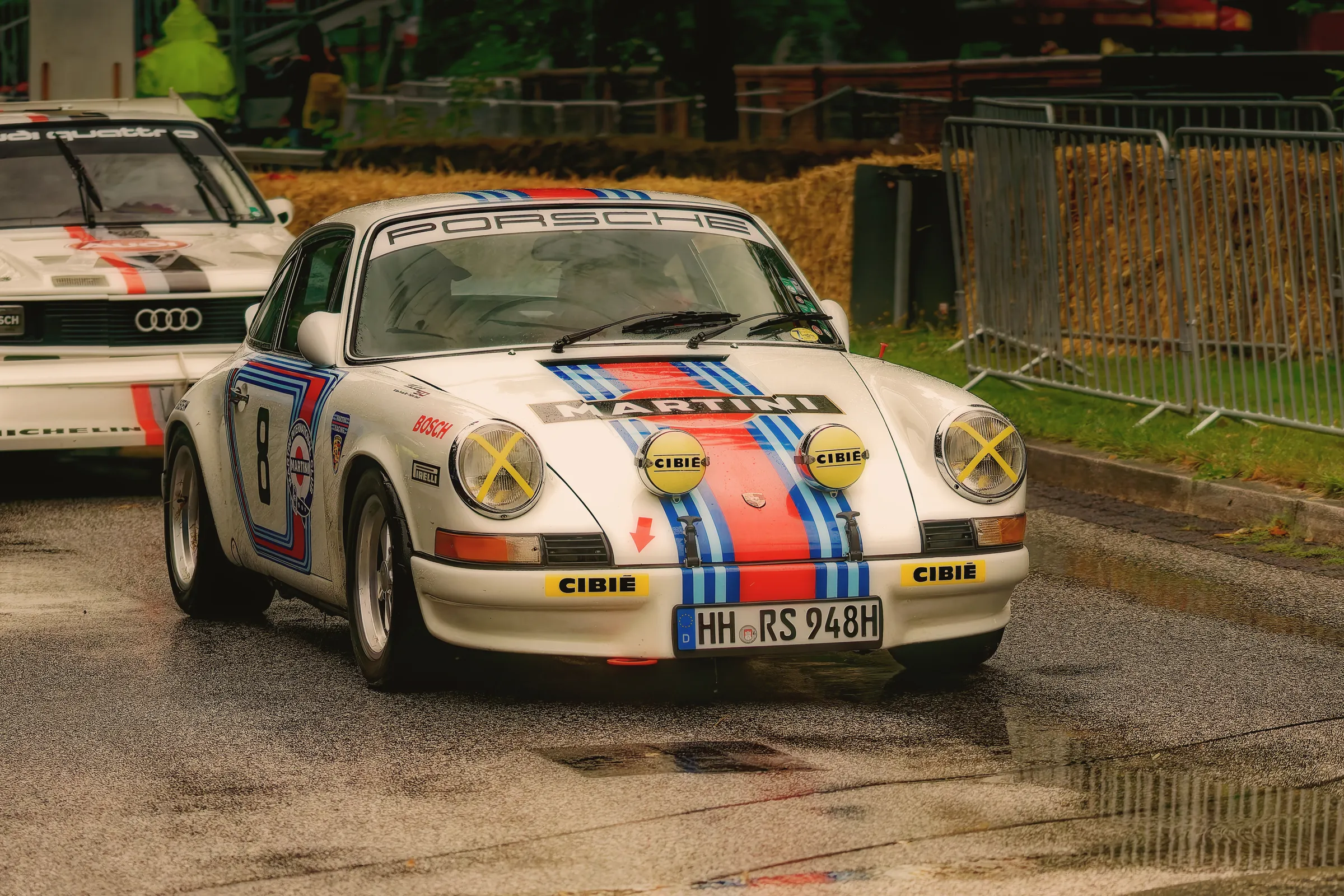Weißer klassischer Porsche 911 im Martini-Racing-Design mit Startnummer 8, Zusatzscheinwerfern und gelben Scheinwerferabdeckungen.