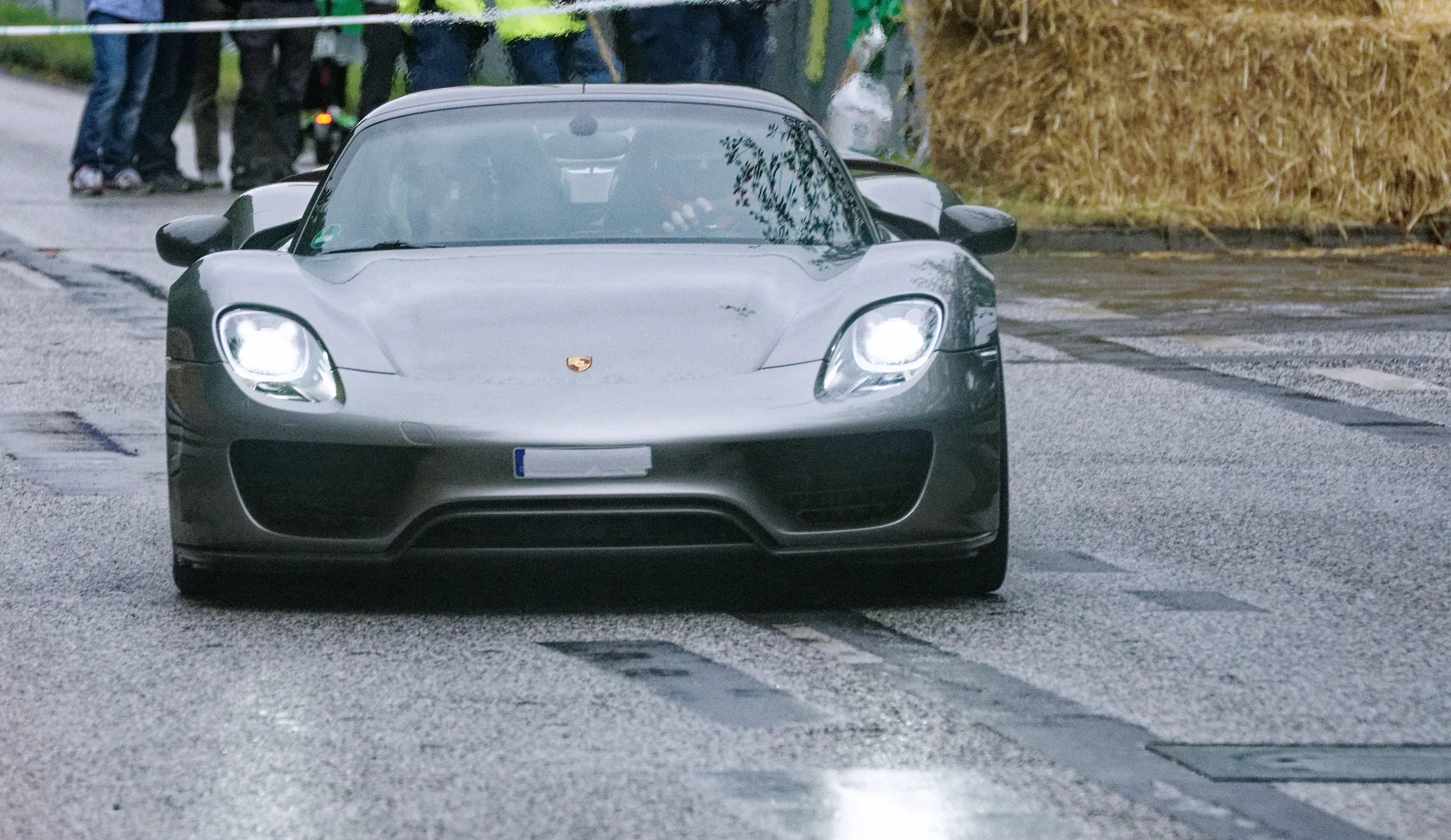 Grauer Porsche 918 Spyder mit eingeschalteten LED-Scheinwerfern auf regennasser Strecke beim Hamburger Stadtpark-Revival.