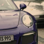 Nahaufnahme der Front eines violetten Porsche 911 GT3 RS mit rundem LED-Scheinwerfer und Regentropfen auf der Motorhaube Nahaufnahme der Front eines violetten Porsche 911 GT3 RS mit rundem LED-Scheinwerfer und Regentropfen auf der Motorhaub