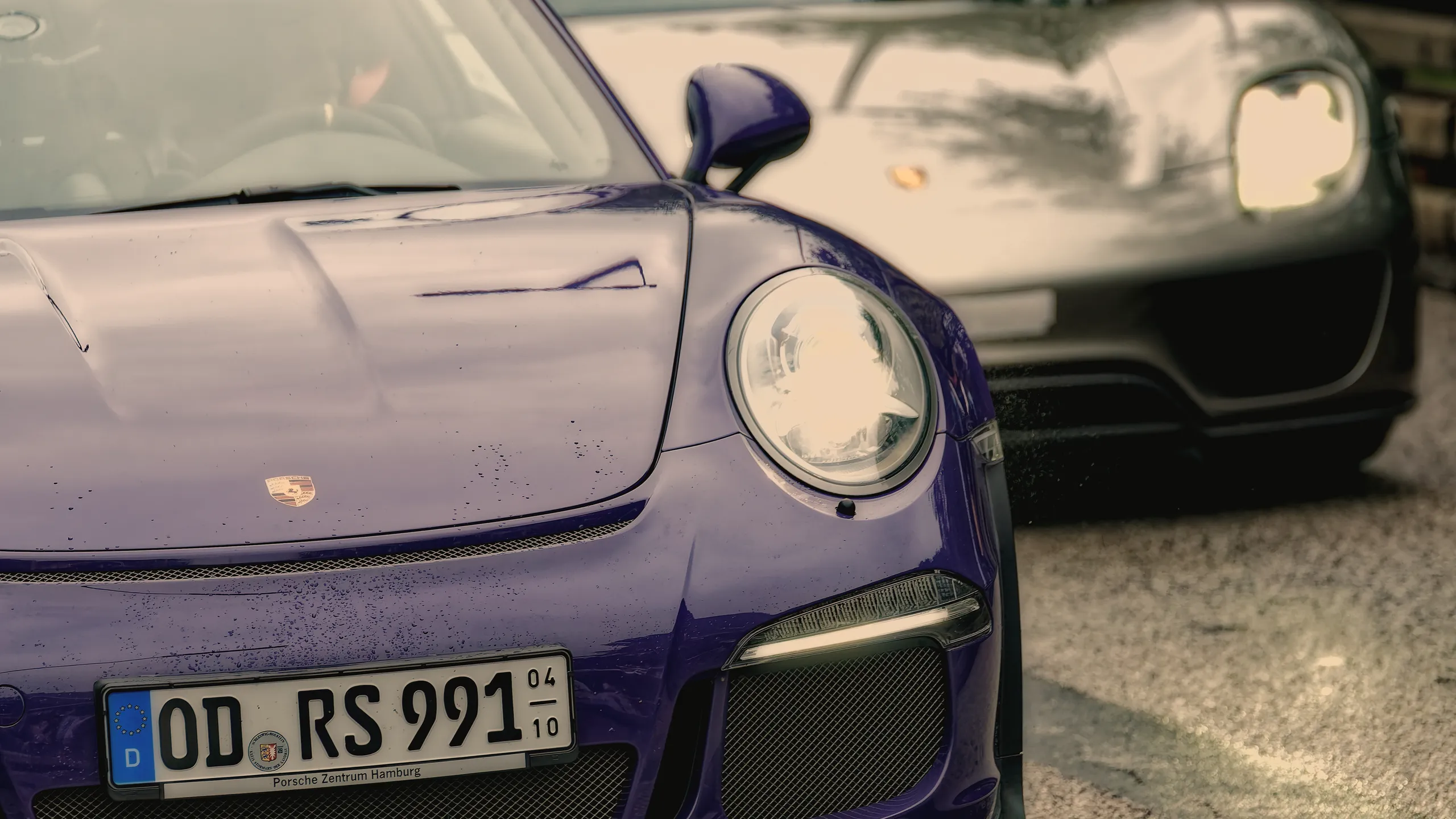 Nahaufnahme der Front eines violetten Porsche 911 GT3 RS mit rundem LED-Scheinwerfer und Regentropfen auf der Motorhaub