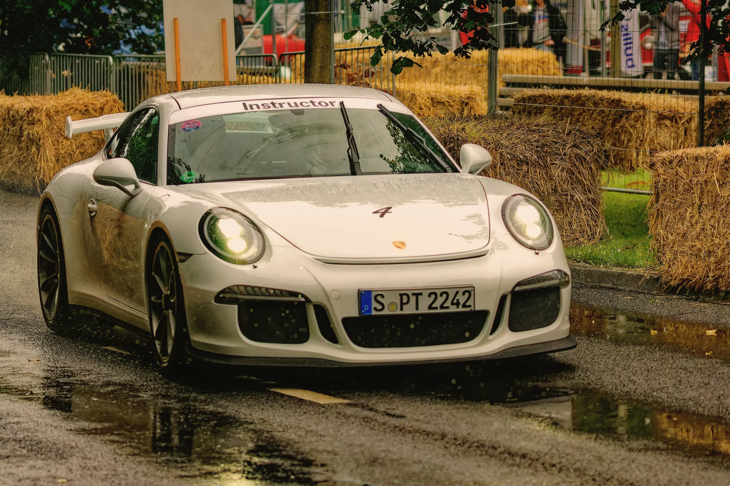 Orangefarbener klassischer Porsche 911 mit Startnummer 266 und schwarzen Felgen auf nasser Rennstrecke in Hamburg.