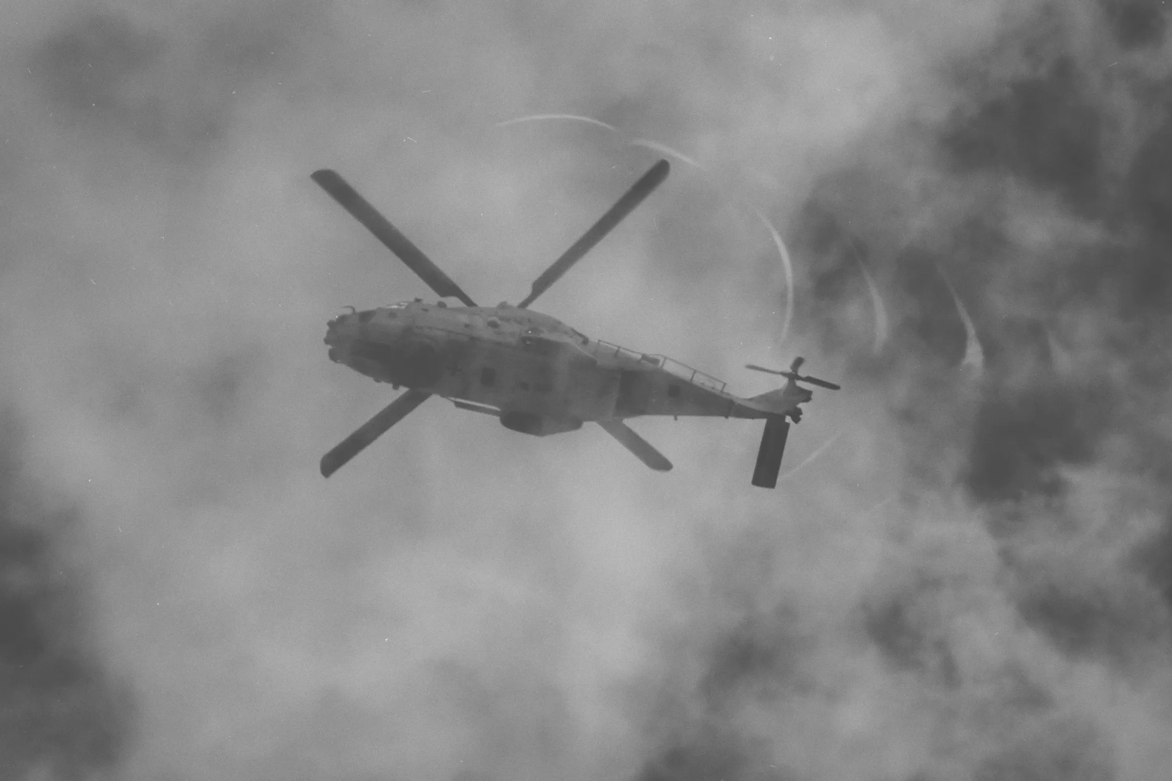 Schwarzweißfotografie eines Militärhubschraubers NH-90 als dunkle Silhouette vor einem wolkenverhangenen Himmel.