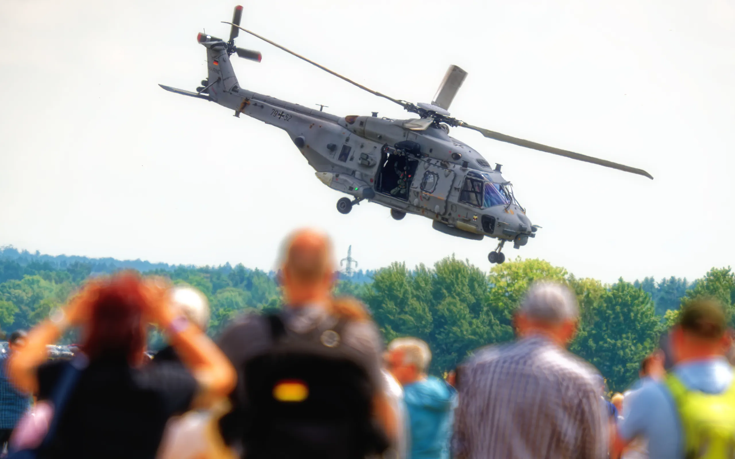 NH90 Sea Lion der Bundeswehr im niedrigen Flug über grünen Baumwipfeln, mit geöffneter Seitentür und sichtbarer Besatzung.