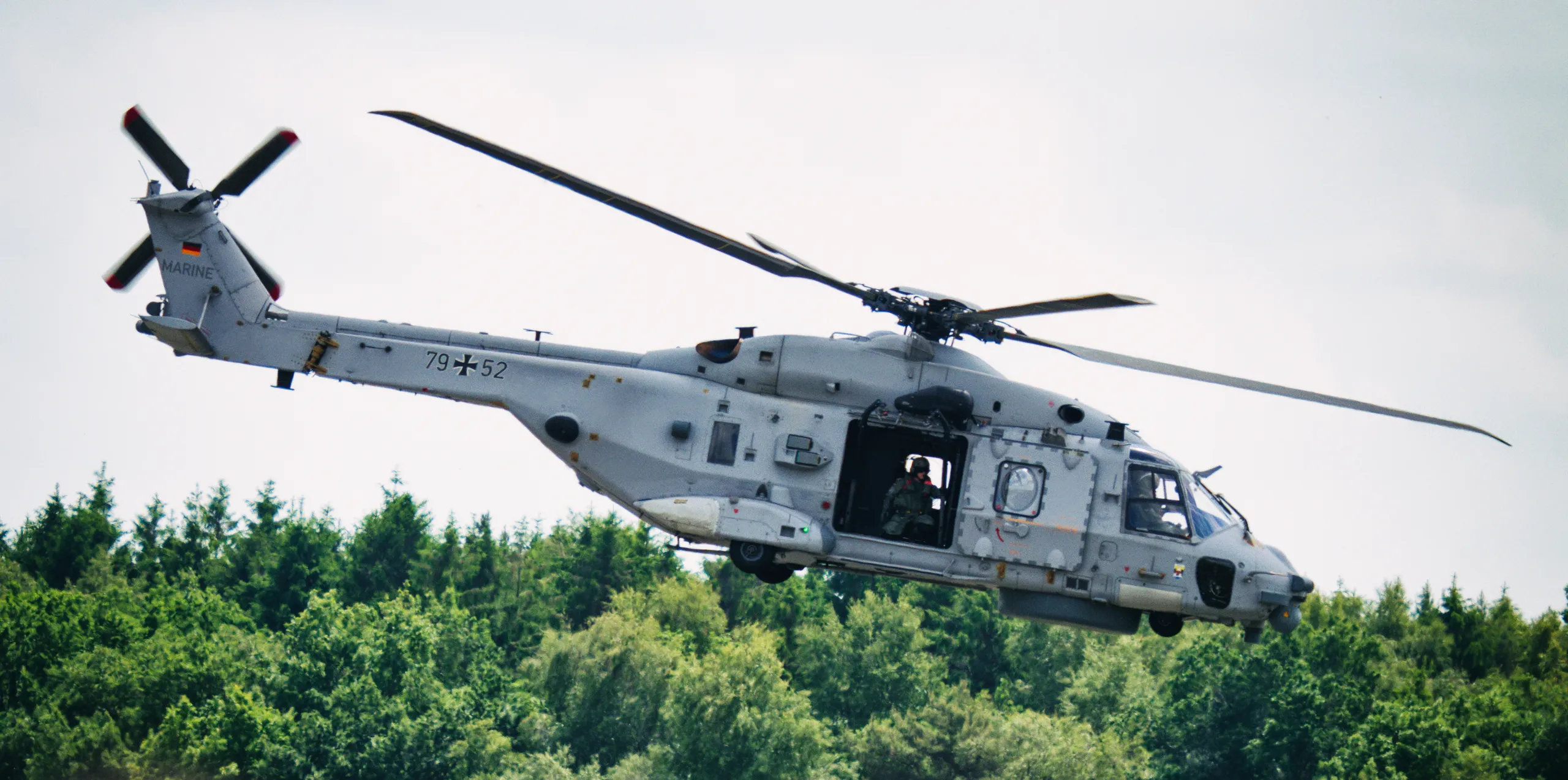 NH90 der Deutschen Marine mit der Kennung 79+52 im Flug mit geöffneter Seitentür und sichtbarem Besatzungsmitglied.