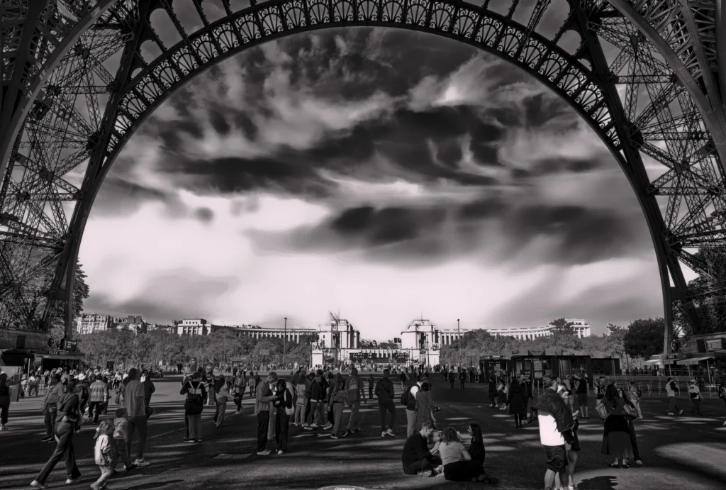 Schwarz-Weiß-Fotografie unter dem Eiffelturm mit Blick auf den Platz und dramatische Wolken