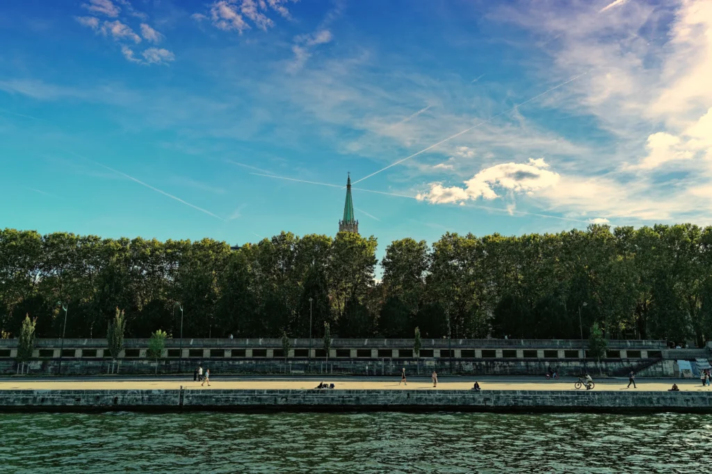 Blick über die Seine auf eine grüne Uferpromenade unter blauem Himmel